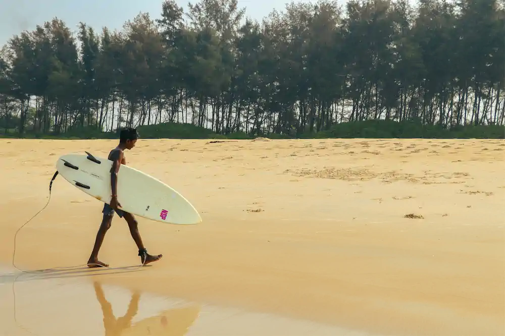 Young surfer carrying a surfboard after training near the shoreline